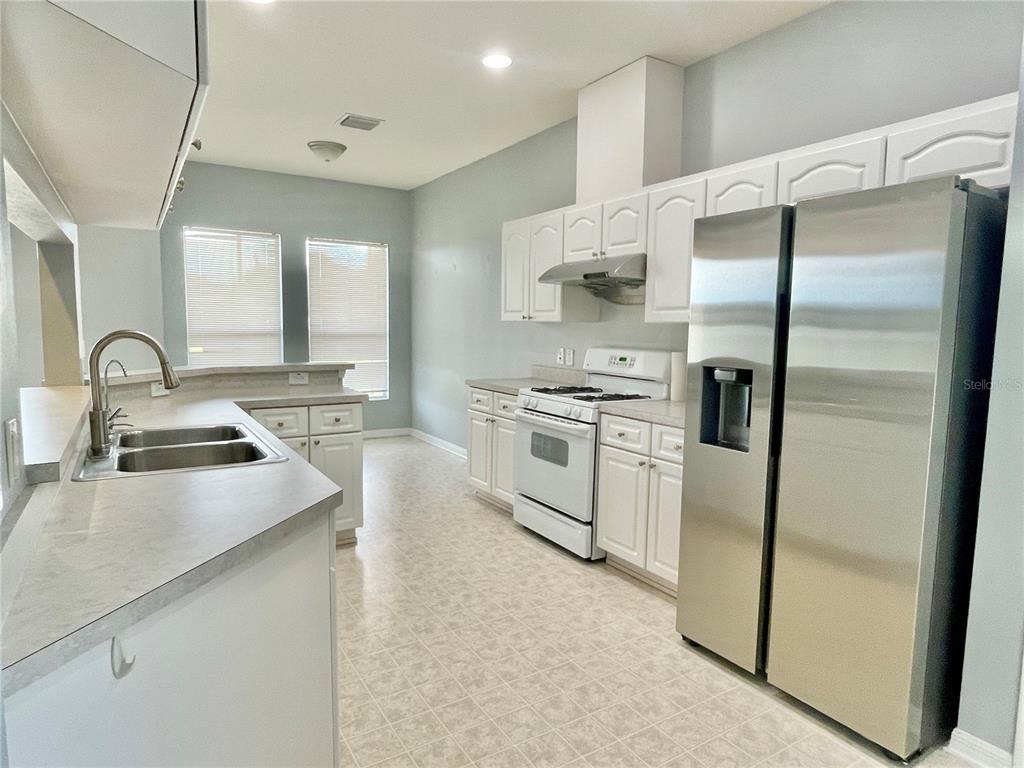A kitchen features white cabinets, stainless steel appliances, a double sink, and light-colored flooring — 24652 PORTOFINO DRIVE, LUTZ, FL