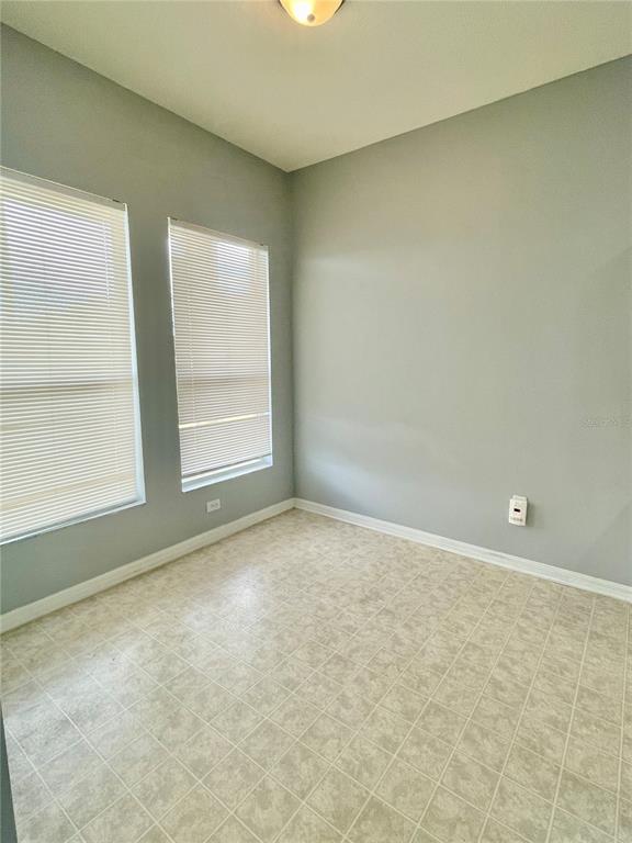 An empty room features light gray walls, two windows with blinds, and tiled flooring — 24652 PORTOFINO DRIVE, LUTZ, FL