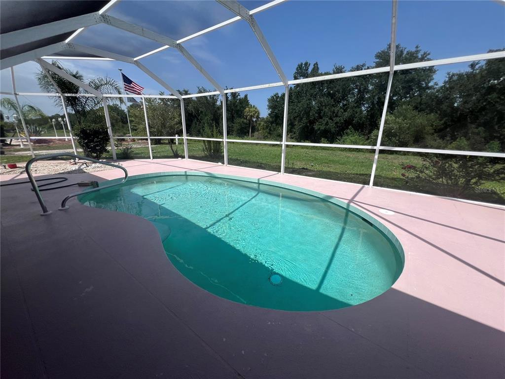 A swimming pool enclosed by a screened lanai overlooks a grassy yard and trees — 2300 MAURITANIA ROAD, PUNTA GORDA, FL