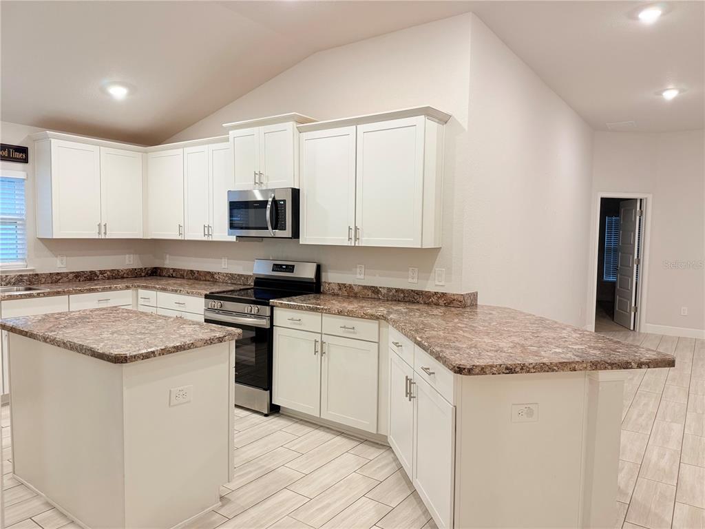 A kitchen features white cabinets, granite countertops, a center island, and stainless steel appliances — 8797 SE 161ST PLACE, SUMMERFIELD, FL