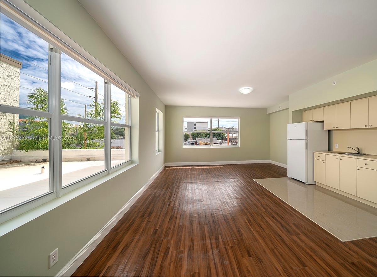 An unfurnished room features wood-look flooring, light green walls, large windows, and a small kitchenette — 804 NW 21st Ter, Miami FL 33127, MIAMI, FL