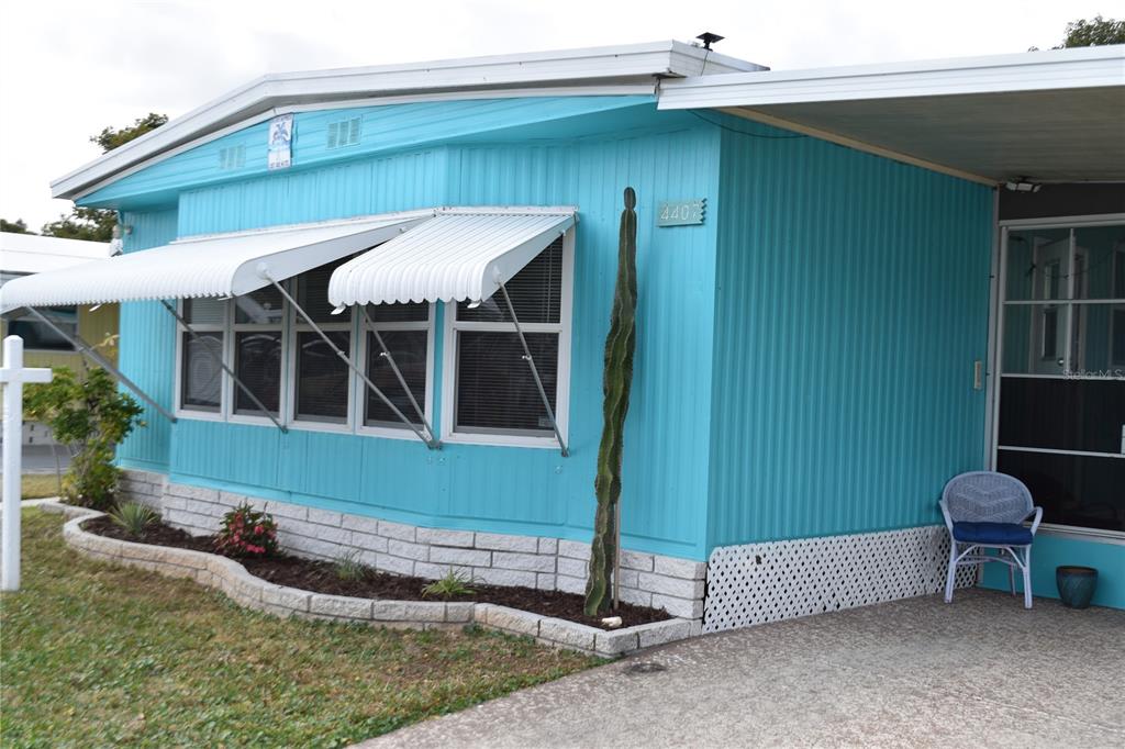 A bright blue mobile home features white metal awnings, a tall cactus, and a concrete driveway — 4407 TUCKER SQUARE, NEW PORT RICHEY, FL