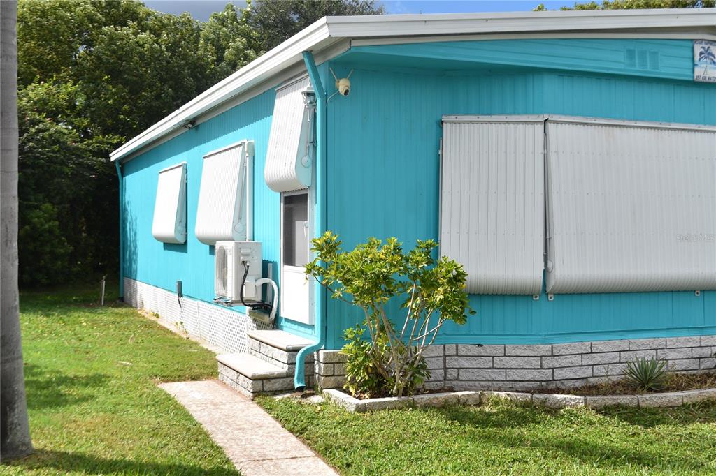 A bright blue mobile home exterior features white metal window awnings and a small staircase — 4407 TUCKER SQUARE, NEW PORT RICHEY, FL