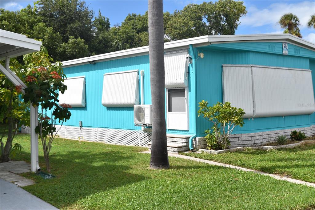 A bright blue mobile home features white metal awnings, a small air conditioning unit, and landscaping — 4407 TUCKER SQUARE, NEW PORT RICHEY, FL