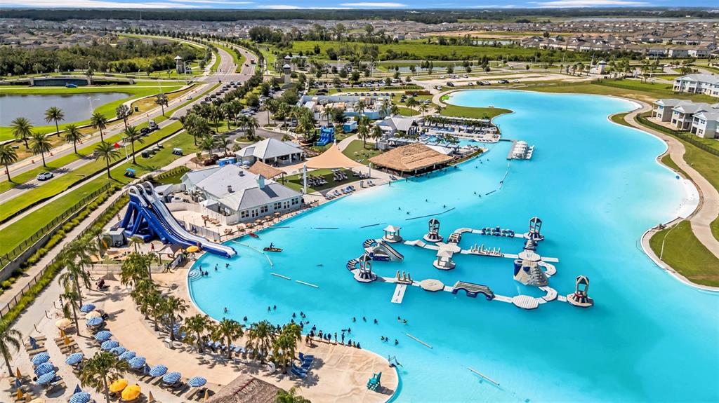An aerial view shows a large turquoise lagoon with an inflatable obstacle course and waterslide — 31440 BARREL WAVE WAY, WESLEY CHAPEL, FL