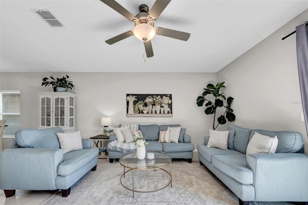 A living room features light blue sofas, a glass coffee table, and a ceiling fan — 31440 BARREL WAVE WAY, WESLEY CHAPEL, FL