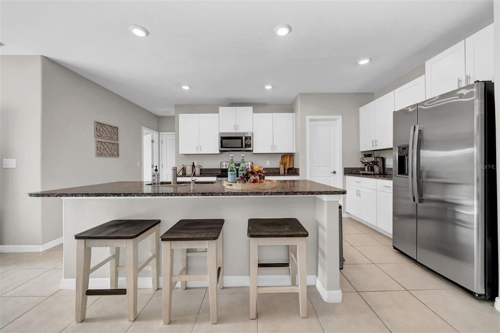 A modern kitchen features white cabinets, granite countertops, a large island, and stainless steel appliances — 31440 BARREL WAVE WAY, WESLEY CHAPEL, FL