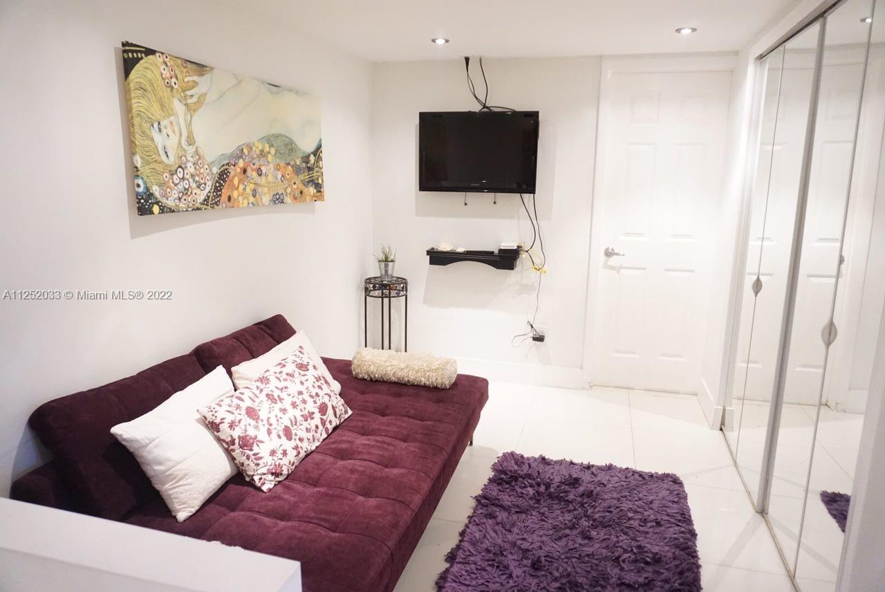 A small room features a purple futon, a wall-mounted television, and white tiled flooring — 5161 COLLINS AV # 309, Miami Beach FL 33140, MIAMI BEACH, FL