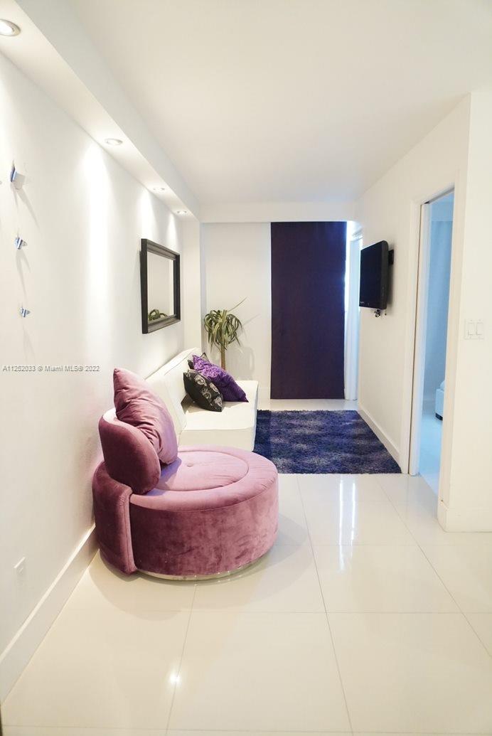 A living room features white walls, a purple circular chair, a white sofa, and tile flooring — 5161 COLLINS AV # 309, Miami Beach FL 33140, MIAMI BEACH, FL
