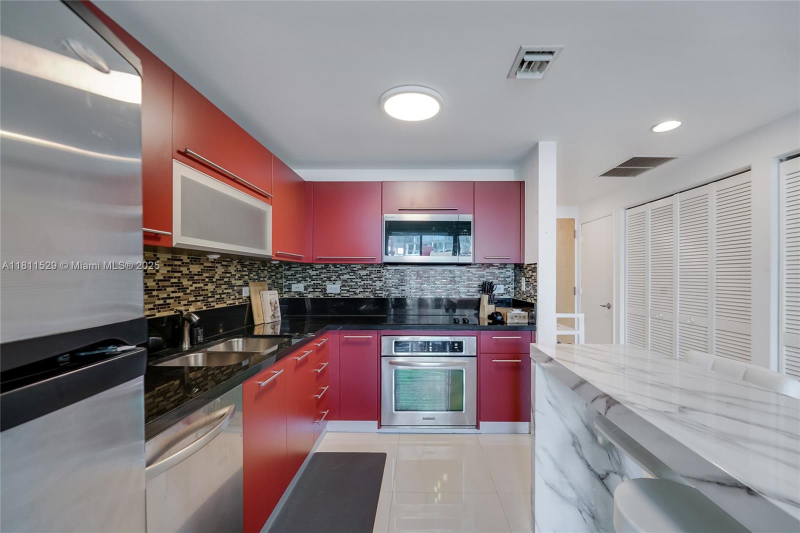A kitchen features red cabinets, black countertops, stainless steel appliances, and a marble-topped island — 244 Biscayne Blvd # 644, Miami FL 33132, MIAMI, FL