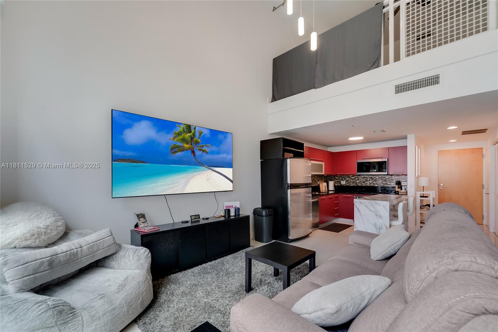A living room with a large television, grey sofa, and an adjacent red-cabinet kitchen — 244 Biscayne Blvd # 644, Miami FL 33132, MIAMI, FL