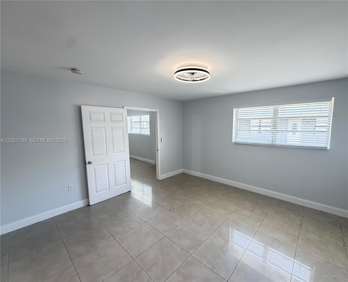 An empty room features light gray walls, large beige floor tiles, and a ceiling fan — HOLLYWOOD, FL