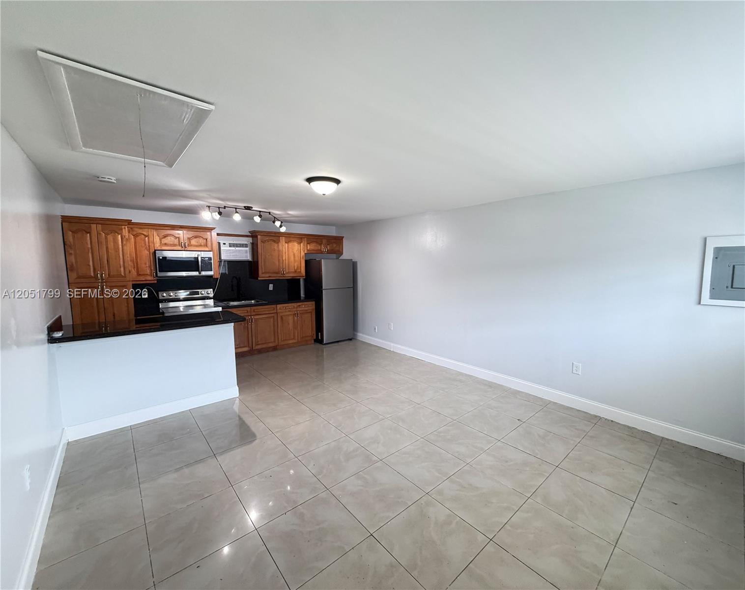 An open-concept kitchen with wood cabinets and tile flooring flows into a living area — HOLLYWOOD, FL