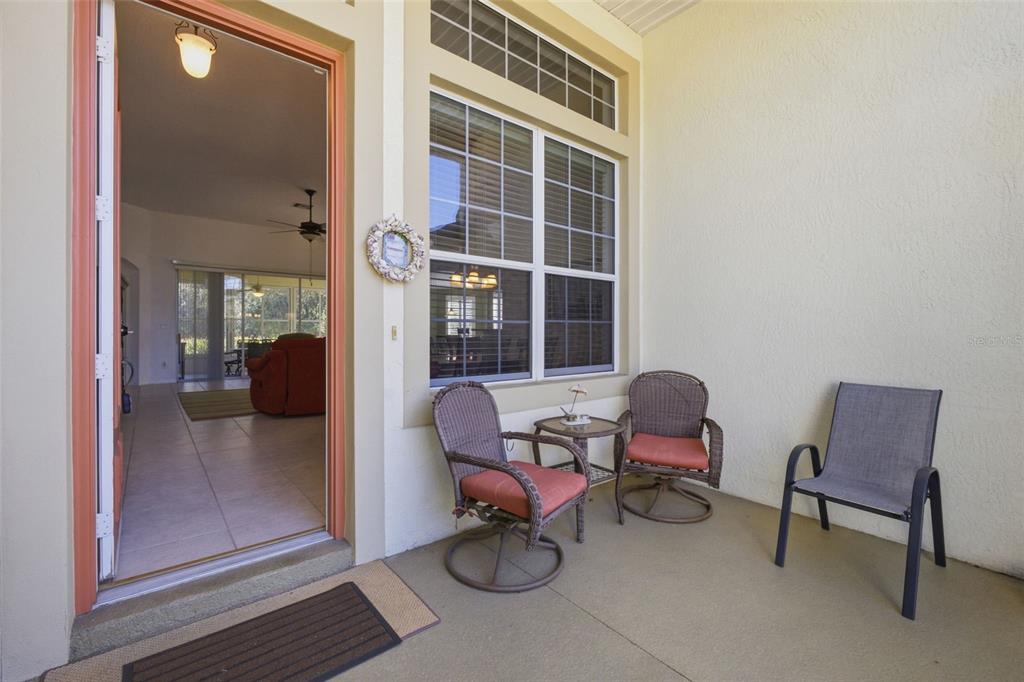A covered patio features three chairs, a small table, and an open doorway to the interior — 5922 SAGE LEAF PLACE, LEESBURG, FL