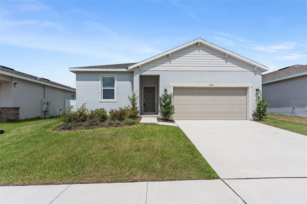 A single-story house with a light gray exterior, a two-car garage, and a front lawn — 1084 PATRIOT LOOP, HAINES CITY, FL