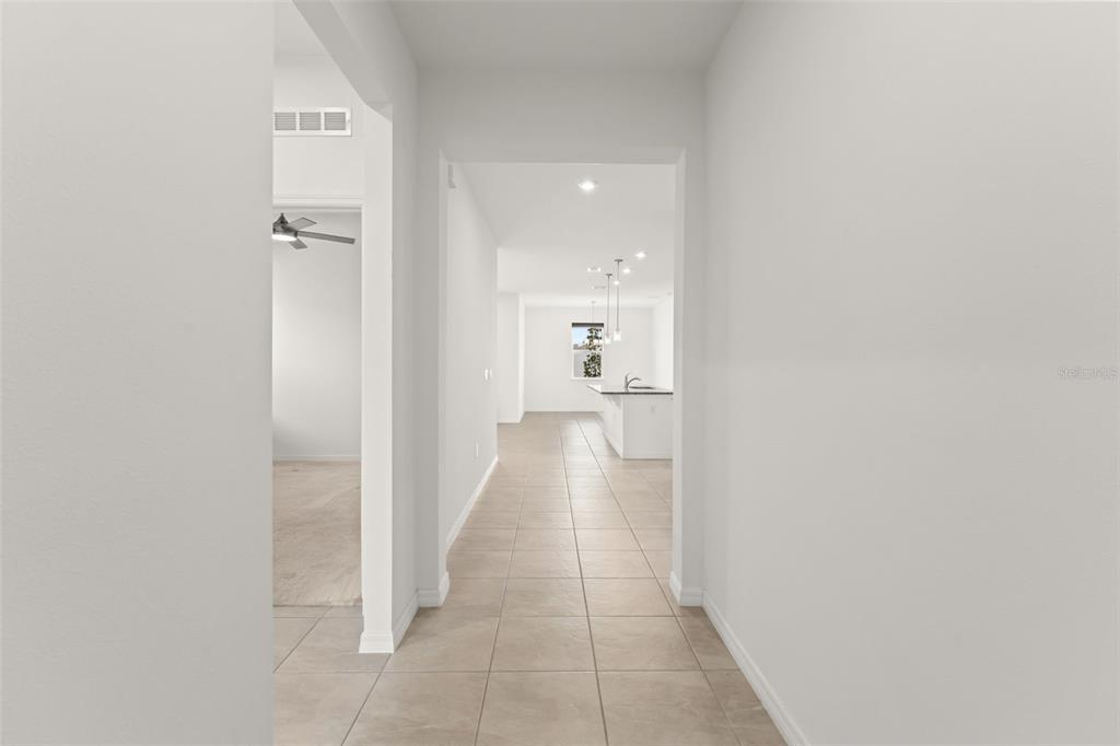 A tiled hallway leads from a neutral-toned entryway toward an open-concept kitchen and living area — 1084 PATRIOT LOOP, HAINES CITY, FL