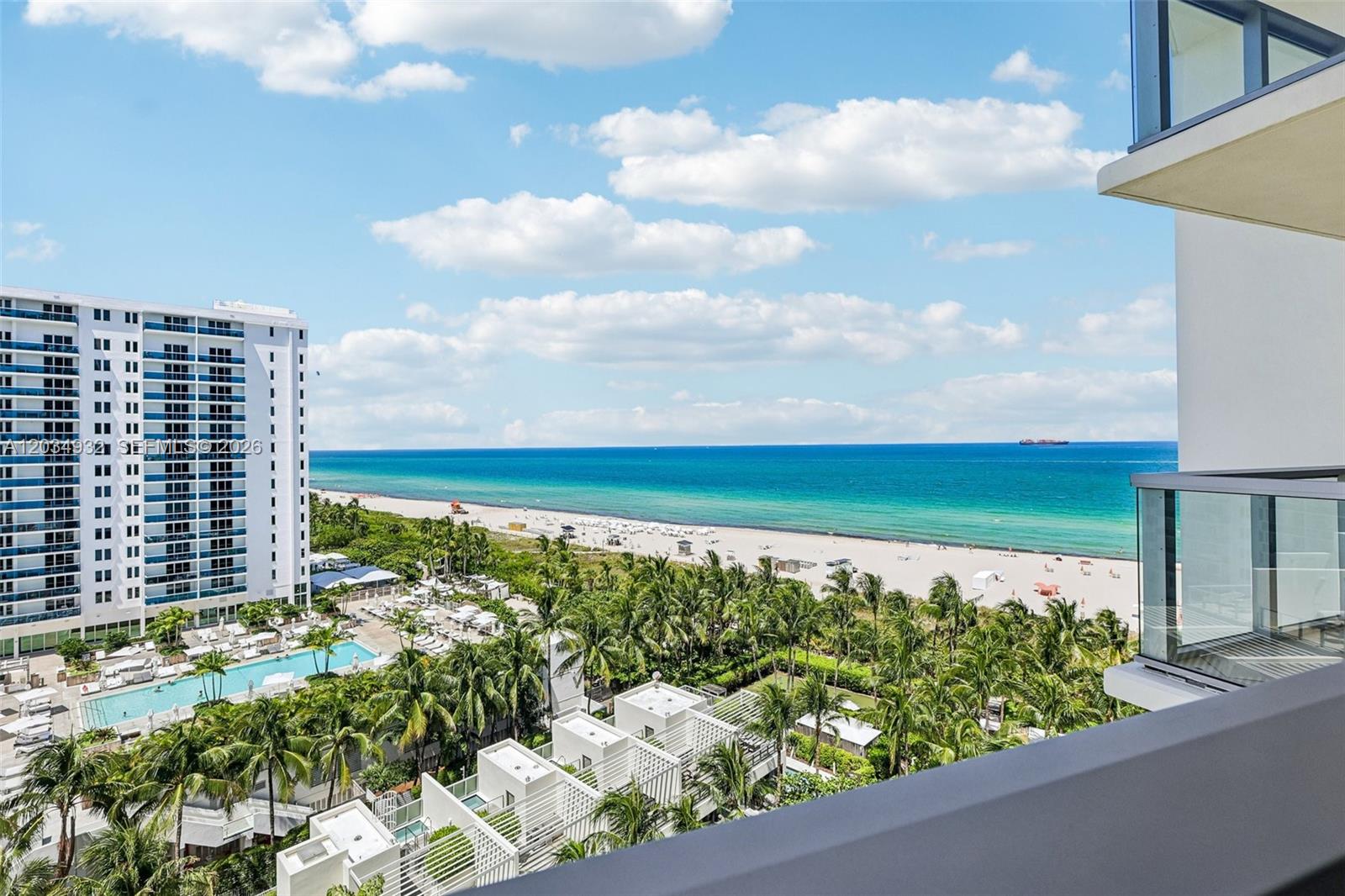 A high-angle view from a balcony overlooking a beach, ocean, and surrounding resort buildings — 2201 Collins Ave # 1019, Miami Beach FL 33139, MIAMI BEACH, FL