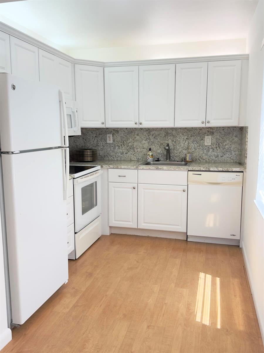 A kitchen features white cabinets, granite countertops, white appliances, and light wood-look flooring — 490 Normandy # K, Delray Beach FL 33484, DELRAY BEACH, FL