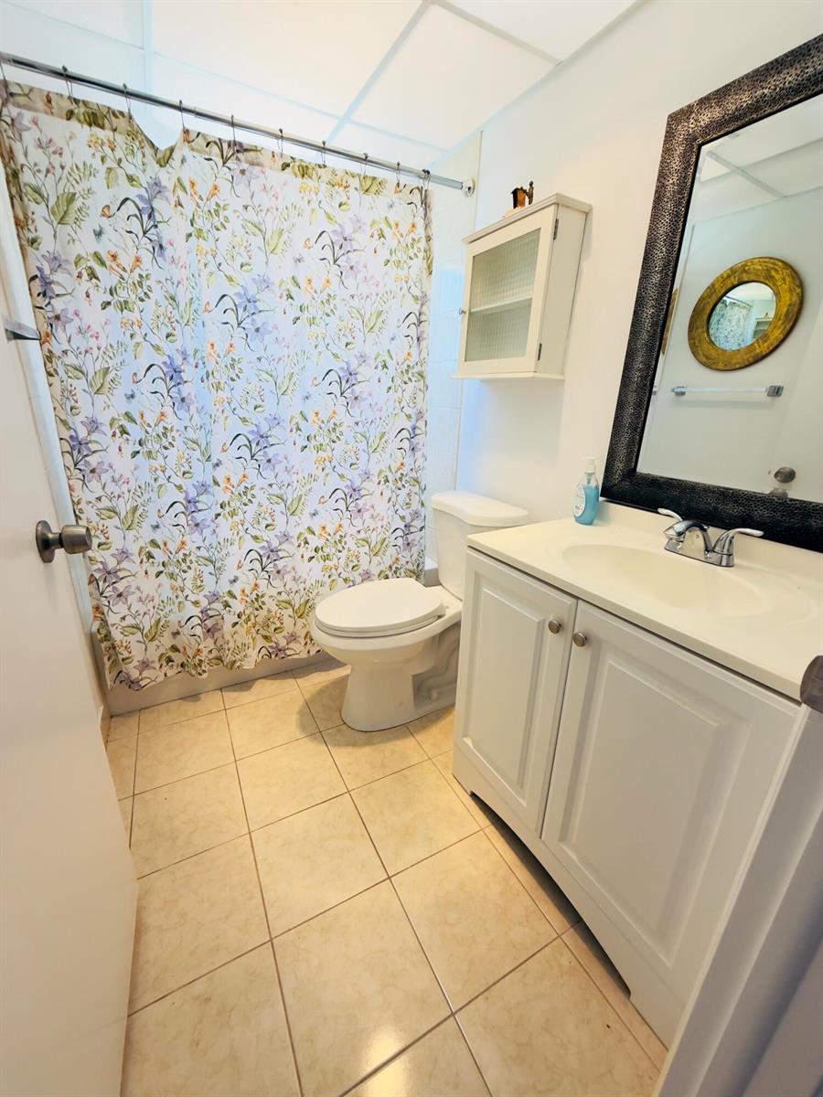 A bathroom features a floral shower curtain, a white vanity, a toilet, and a mirror — 490 Normandy # K, Delray Beach FL 33484, DELRAY BEACH, FL