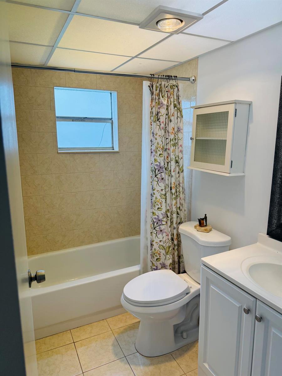 A bathroom featuring a tub-shower combination with beige tile, a toilet, and a white vanity — 490 Normandy # K, Delray Beach FL 33484, DELRAY BEACH, FL