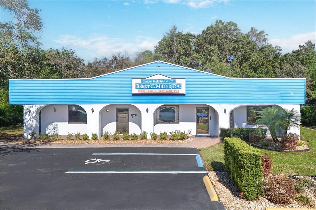 An aerial view shows a commercial building with a parking lot and surrounding trees — 205 E BURLEIGH BOULEVARD, TAVARES, FL