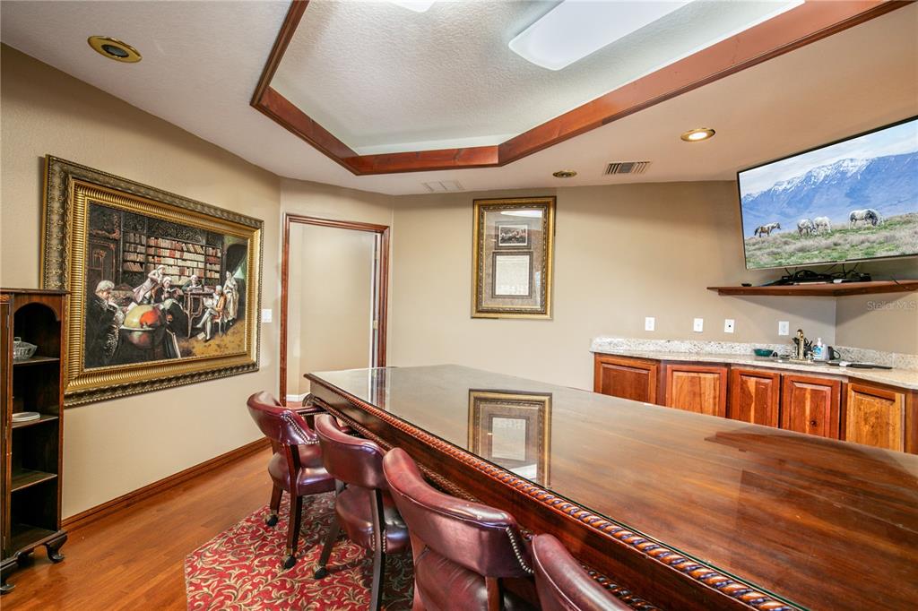 A home bar area features a long wooden counter, leather stools, and decorative framed artwork — 205 E BURLEIGH BOULEVARD, TAVARES, FL