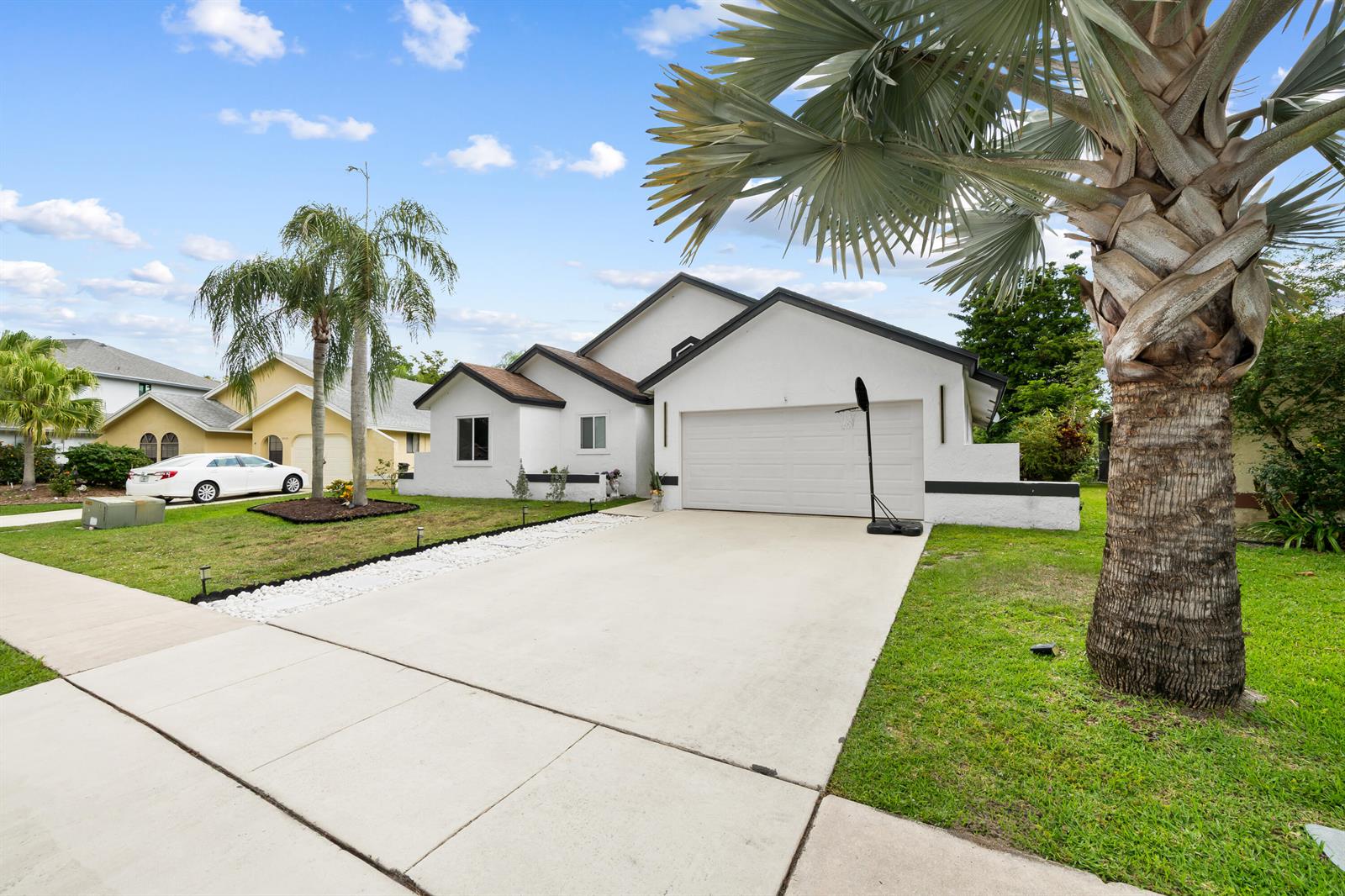 A white single-story house with a two-car garage and a large palm tree in front — 22448 Swordfish Drive, Boca Raton FL 33428, BOCA RATON, FL