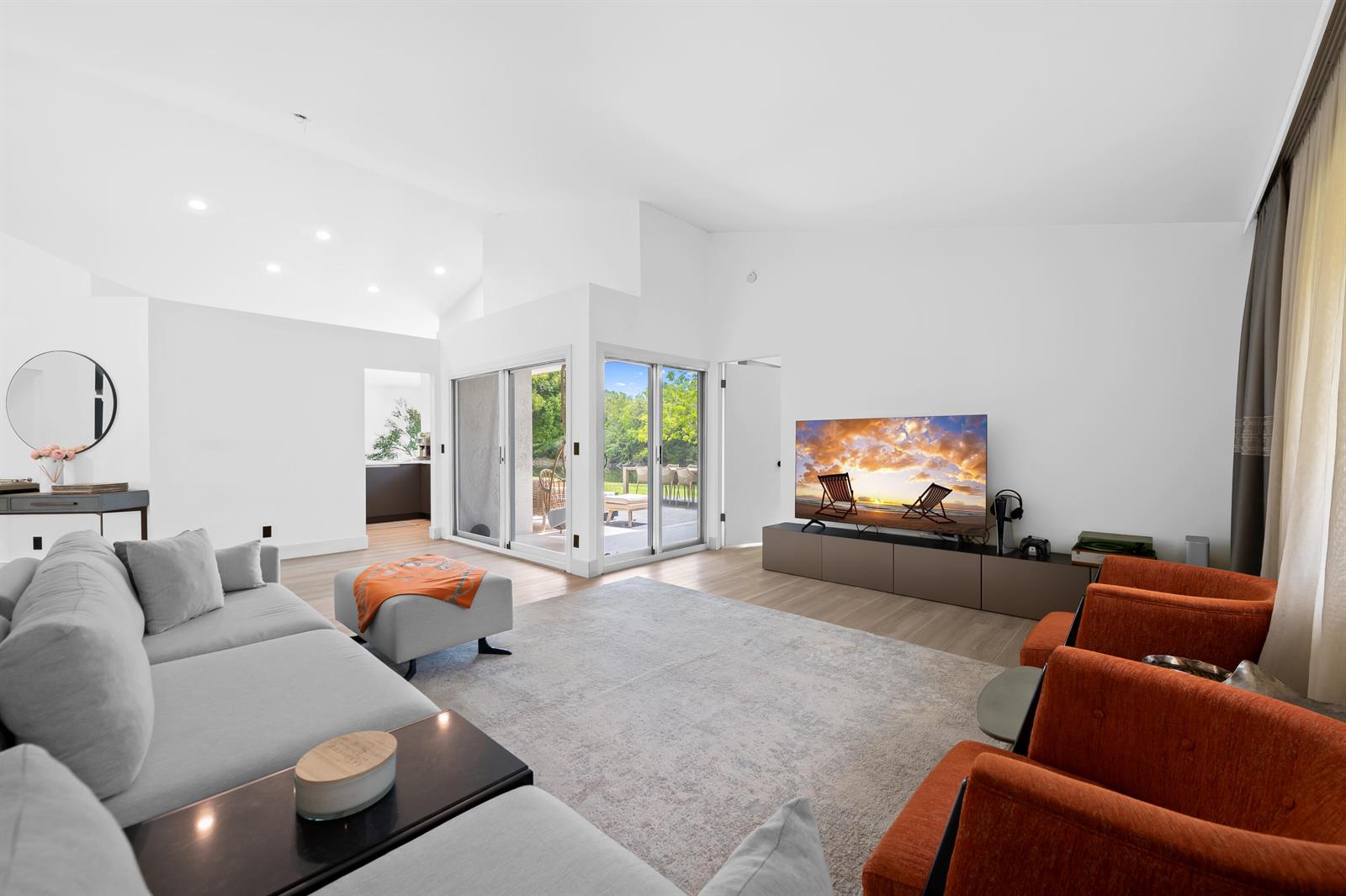 A living room features a grey sectional, orange armchairs, a television, and sliding glass doors — 22448 Swordfish Drive, Boca Raton FL 33428, BOCA RATON, FL