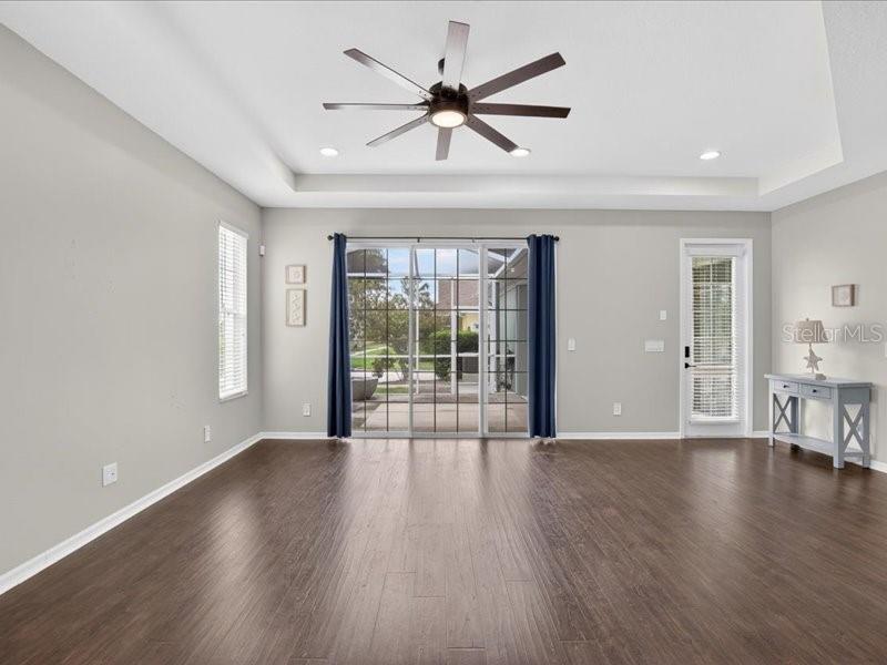A spacious living room features dark wood flooring, a tray ceiling, and a sliding glass door — 5513 GOLDEN ISLES DRIVE, APOLLO BEACH, FL