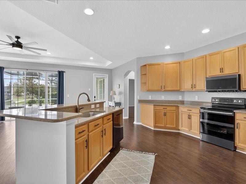 A kitchen features light wood cabinets, a granite island, and dark wood-look flooring — 5513 GOLDEN ISLES DRIVE, APOLLO BEACH, FL