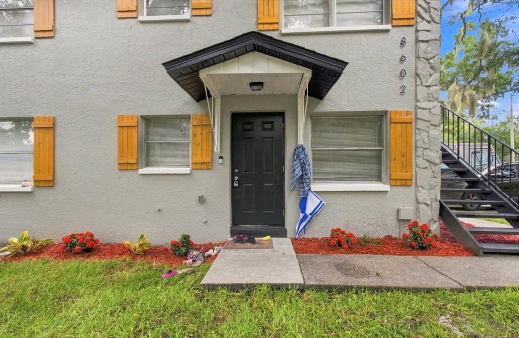 The exterior of a gray apartment building features a black front door and wooden shutters — 8602 N 14TH STREET, TAMPA, FL