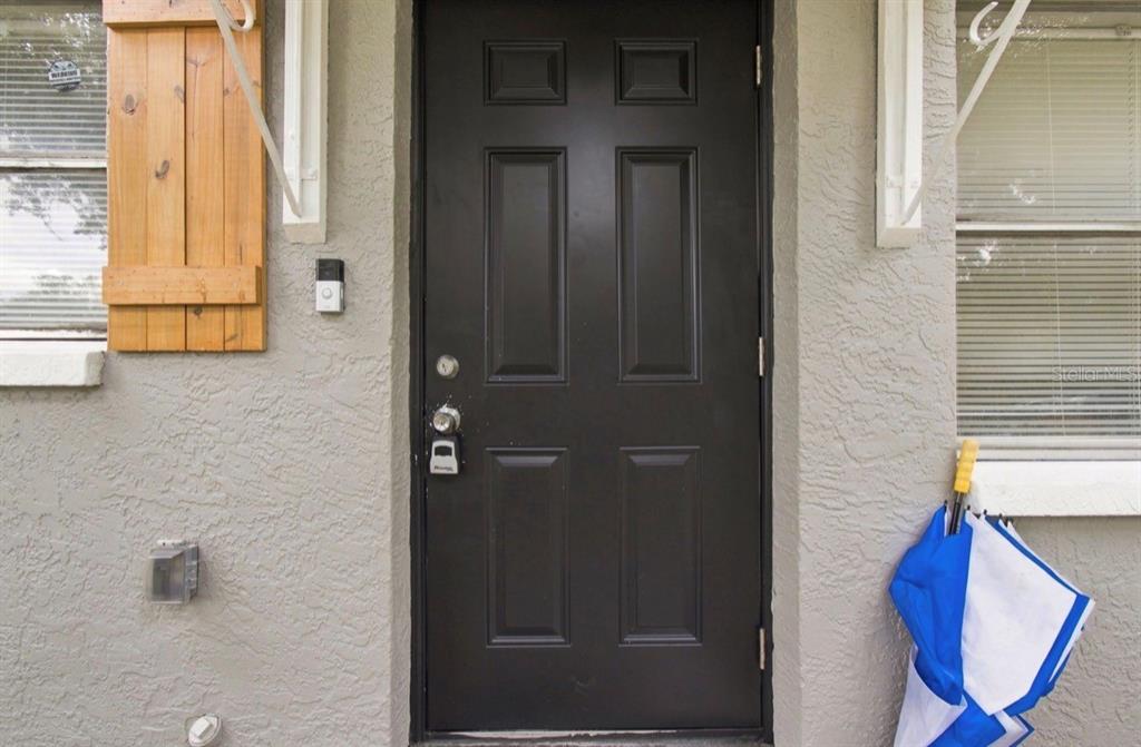 A black front door with a smart doorbell is set into a gray stucco exterior wall — 8602 N 14TH STREET, TAMPA, FL