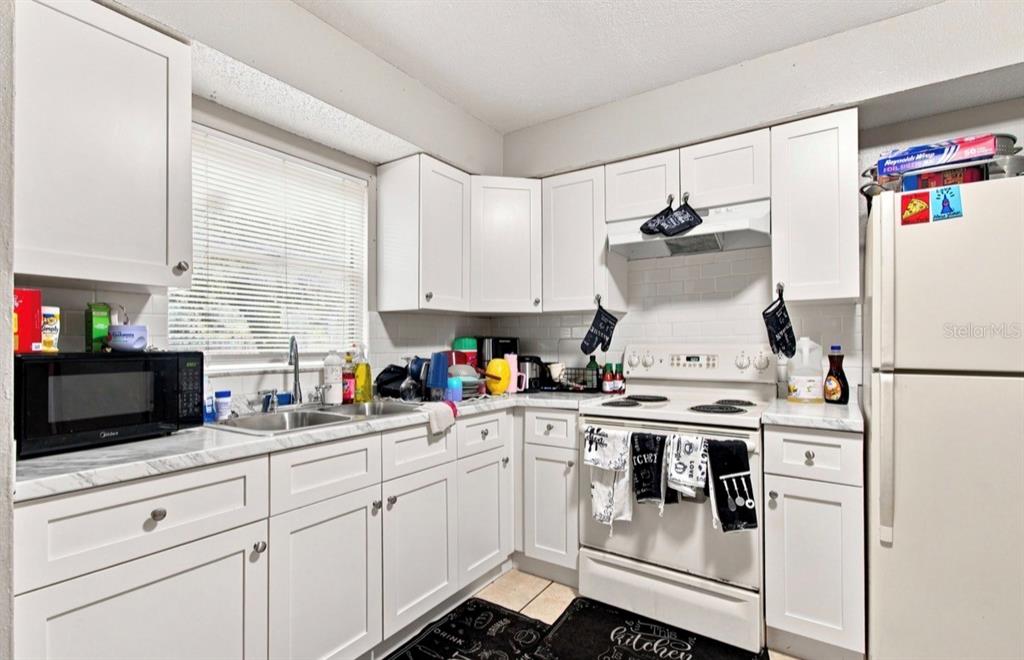 A kitchen with white cabinets, a white stove, a microwave, and a stainless steel sink — 8602 N 14TH STREET, TAMPA, FL