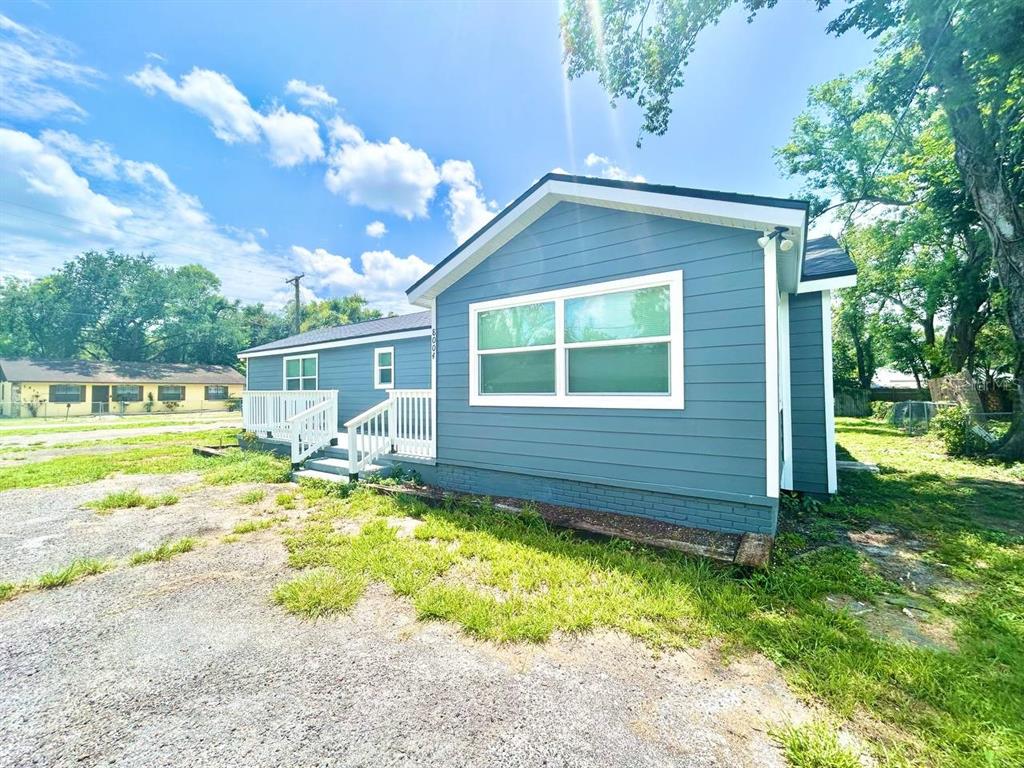 A blue-sided house with a white porch and a gravel yard under a sunny sky — 8004 N MARKS STREET, TAMPA, FL