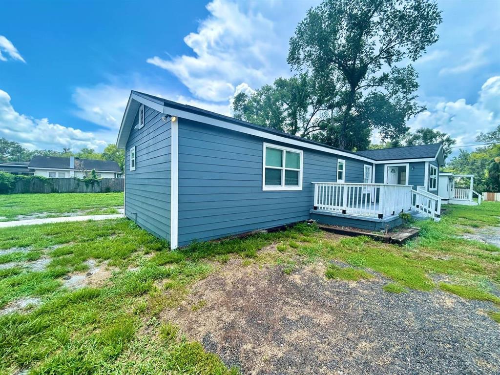 A blue-sided house features a white wooden deck and a gravel driveway under a sky — 8004 N MARKS STREET, TAMPA, FL