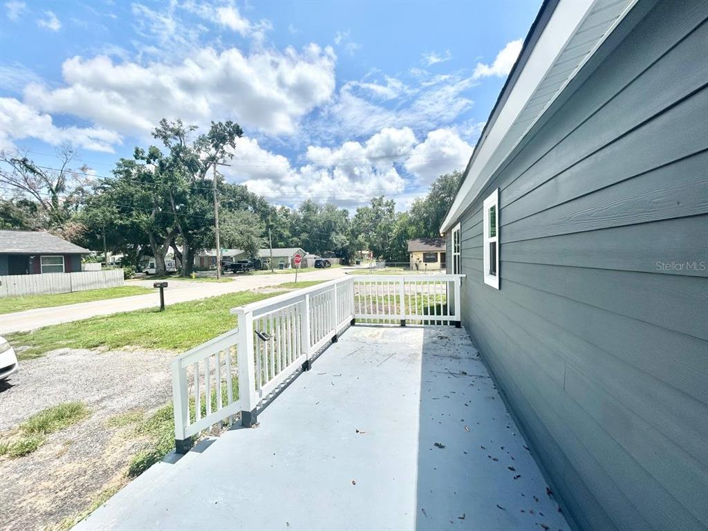 A gray-sided house features a covered porch with white railings overlooking a gravel driveway — 8004 N MARKS STREET, TAMPA, FL