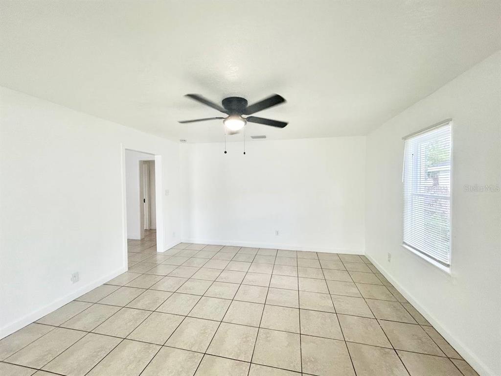 A bright, empty room features white walls, a ceiling fan, and light-colored tile flooring — 8004 N MARKS STREET, TAMPA, FL