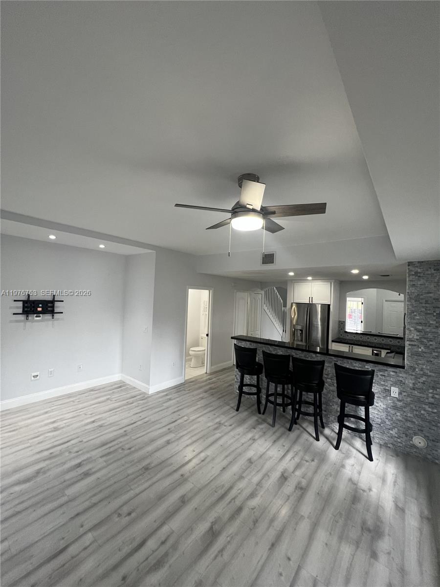 A living room with light wood-look flooring features a breakfast bar and a ceiling fan — 9000 W Flagler St # 1, Miami FL 33174, MIAMI, FL