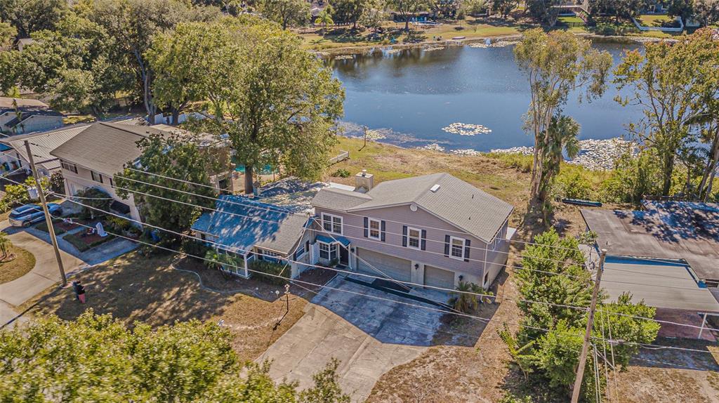 An aerial view shows a two-story house with a gray exterior, attached garage, and lakefront backyard — 12510 FOREST HILLS DRIVE, TAMPA, FL