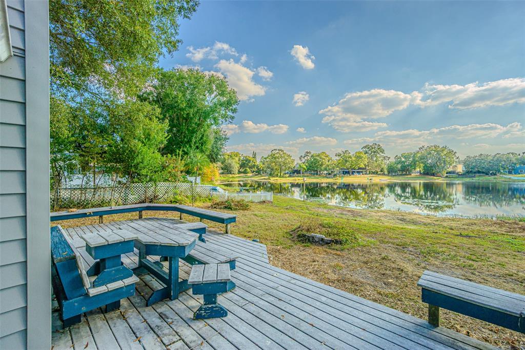 A wooden deck with built-in seating overlooks a lake and a grassy yard — 12510 FOREST HILLS DRIVE, TAMPA, FL