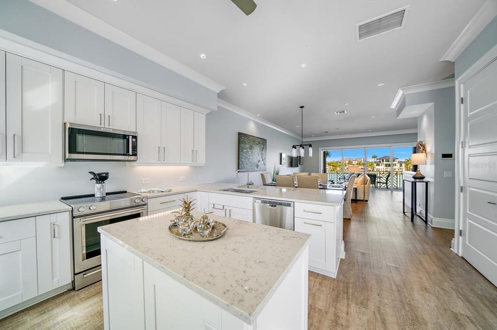 A modern white kitchen with a center island overlooks a dining area and outdoor balcony — 158 BRIGHTWATER DRIVE UNIT 2, CLEARWATER BEACH, FL