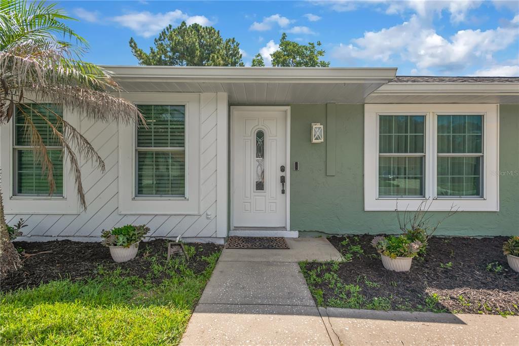 The exterior of a house features a white front door, green siding, and two windows — 819 JACARANDA DRIVE, OLDSMAR, FL