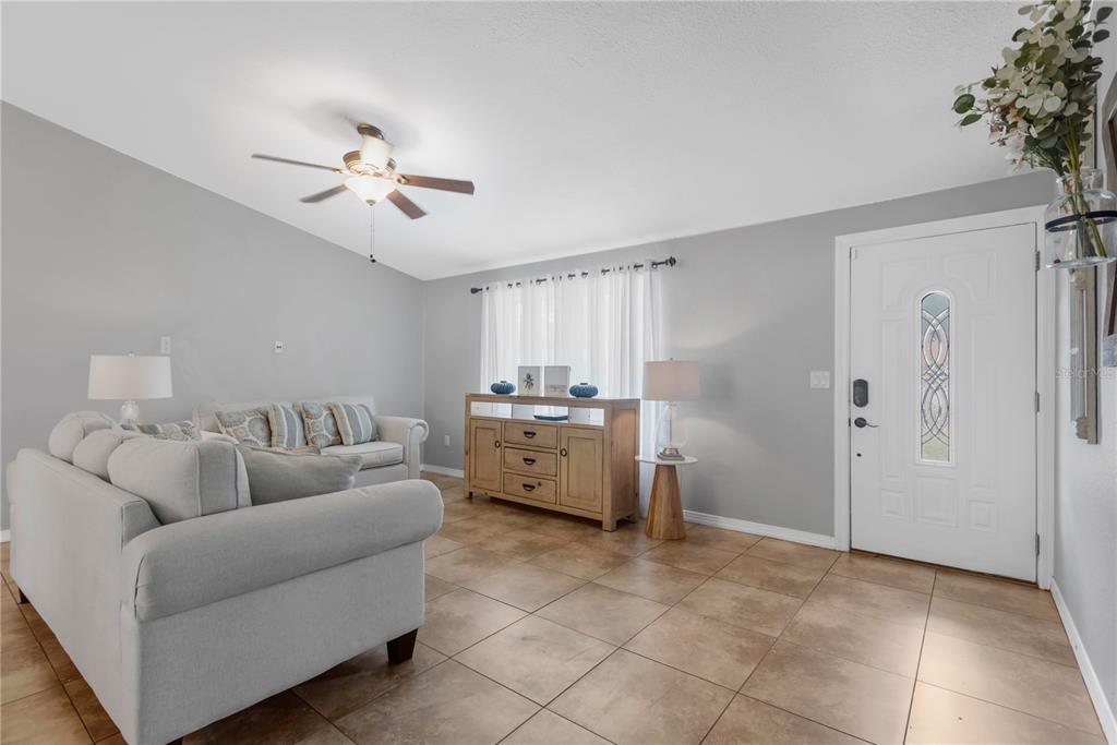 A living room features light gray walls, tile flooring, a white sofa, and a wooden sideboard — 819 JACARANDA DRIVE, OLDSMAR, FL