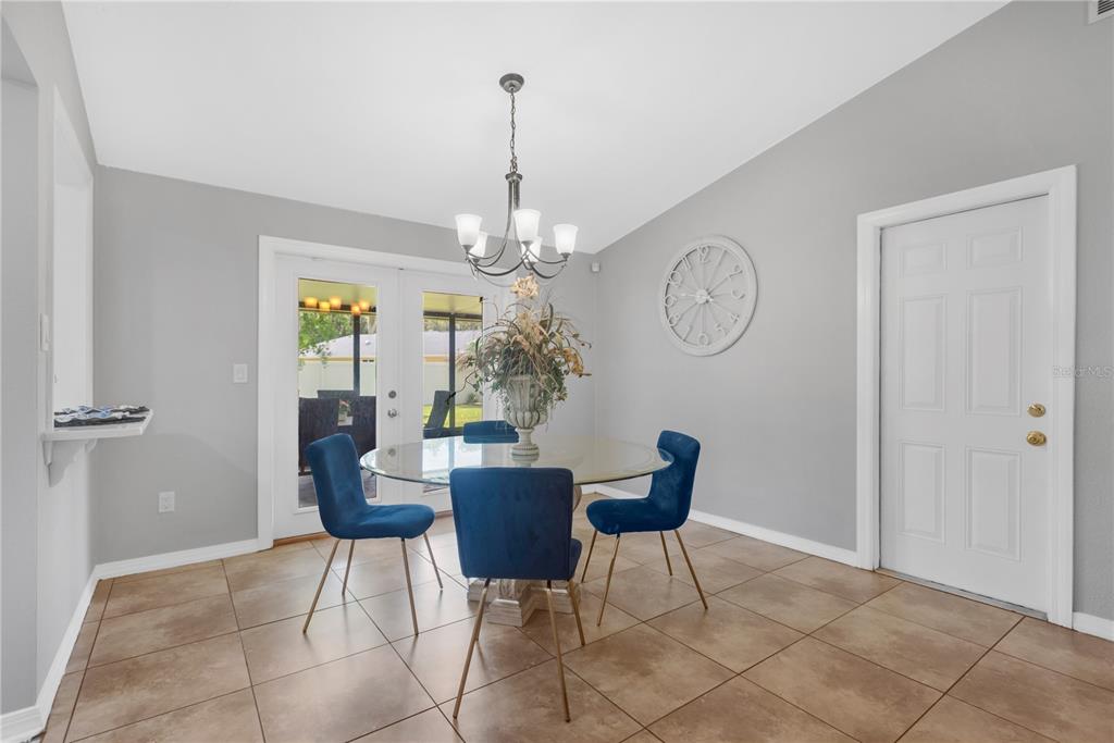 A dining room features a glass-topped table, blue velvet chairs, tile flooring, and a chandelier — 819 JACARANDA DRIVE, OLDSMAR, FL
