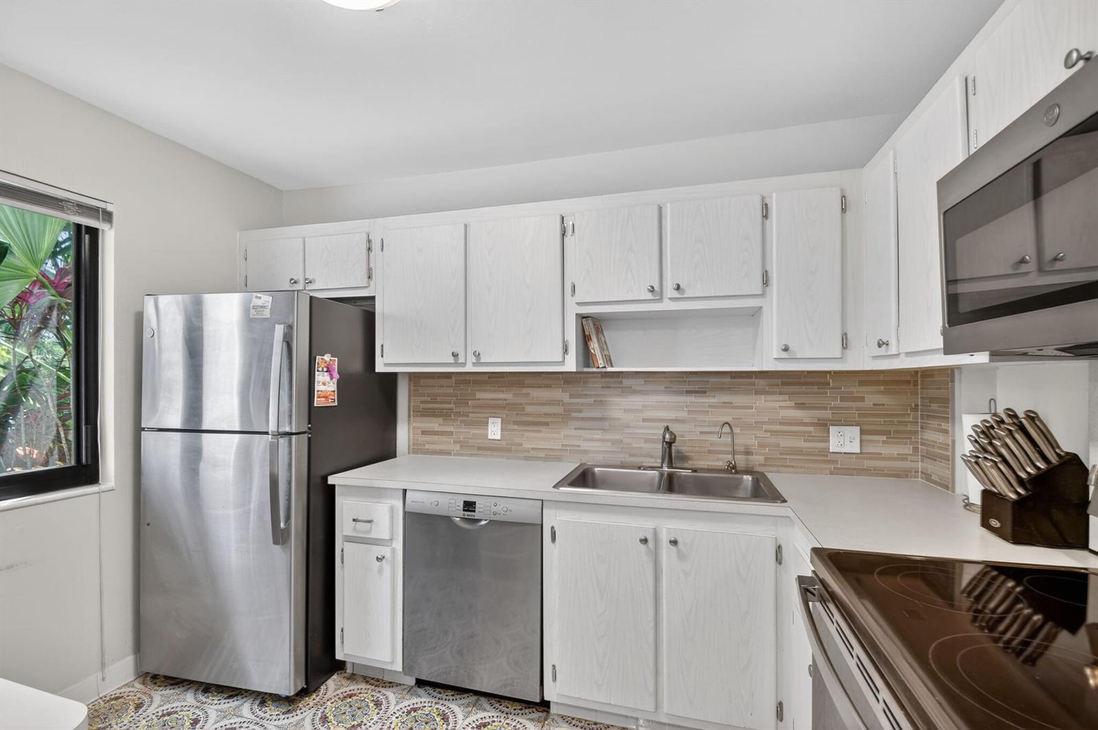 A kitchen features white cabinets, stainless steel appliances, a tiled backsplash, and patterned floor tiles — 4272 Deste Court # 101, Lake Worth FL 33467, LAKE WORTH, FL