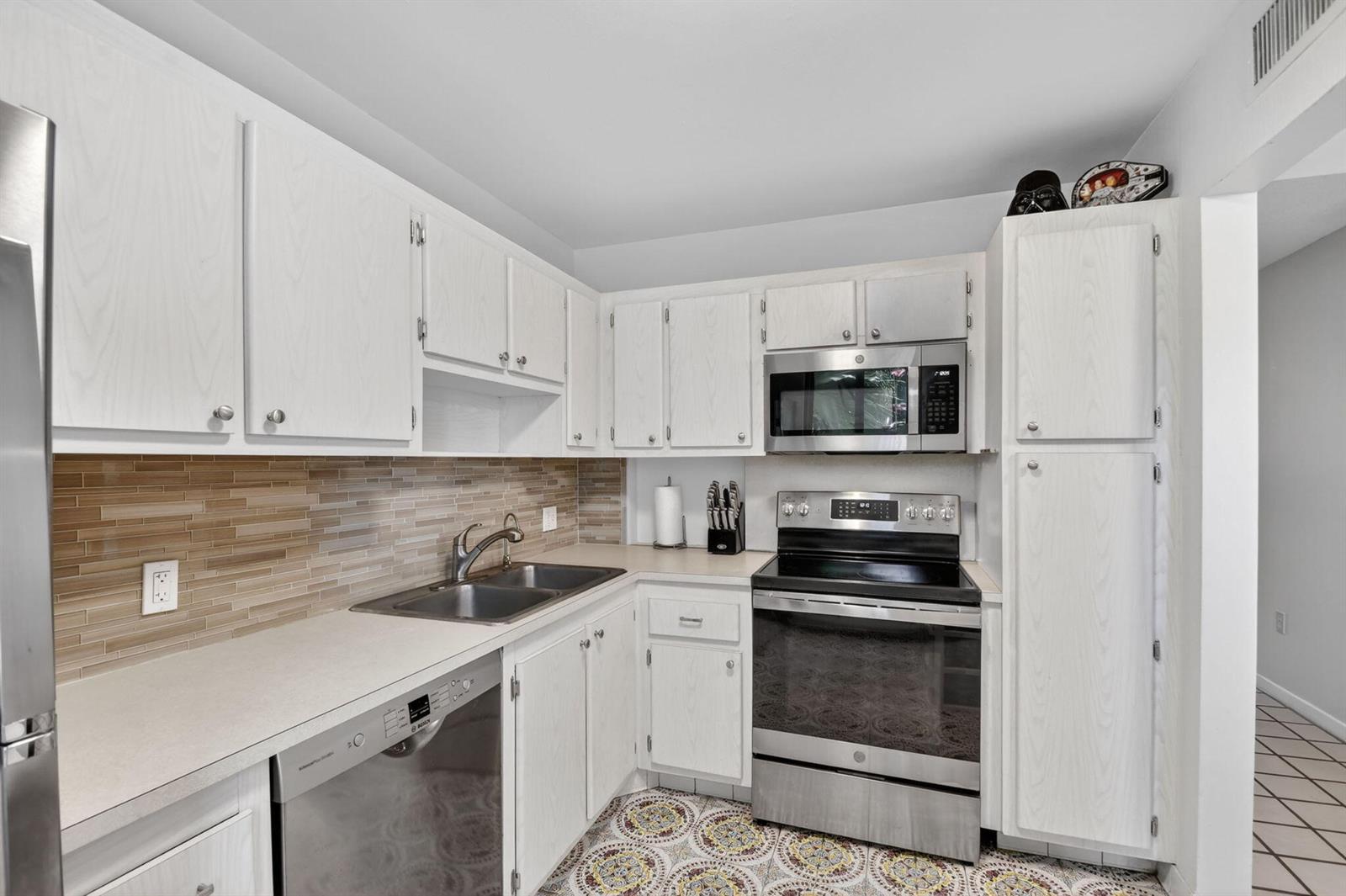 A kitchen features white cabinets, stainless steel appliances, a tiled backsplash, and patterned floor tiles — 4272 Deste Court # 101, Lake Worth FL 33467, LAKE WORTH, FL