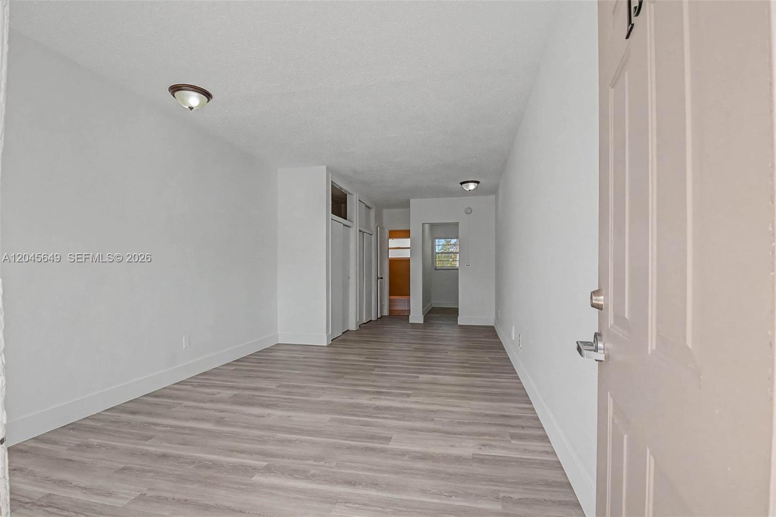 This interior view shows a room with light wood-look flooring, white walls, and closet doors — 1685 Jefferson Ave # 15, Miami Beach FL 33139, MIAMI BEACH, FL