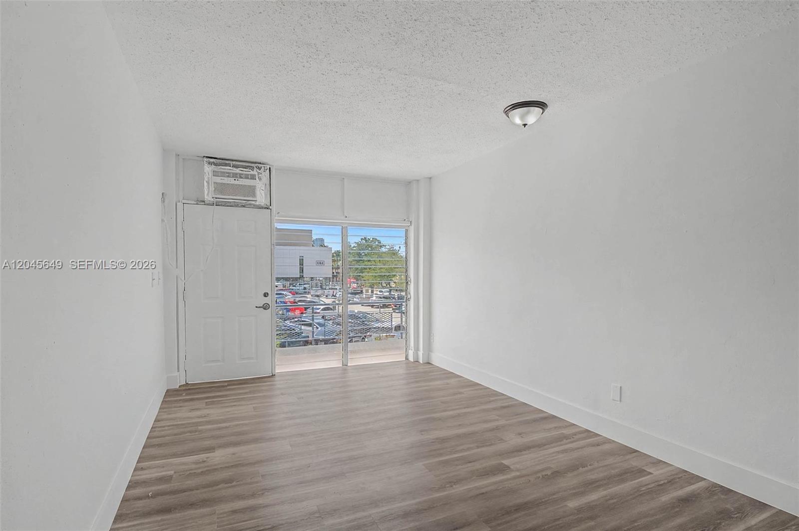 An empty room features white walls, wood-look flooring, a ceiling light, and a balcony door — 1685 Jefferson Ave # 15, Miami Beach FL 33139, MIAMI BEACH, FL
