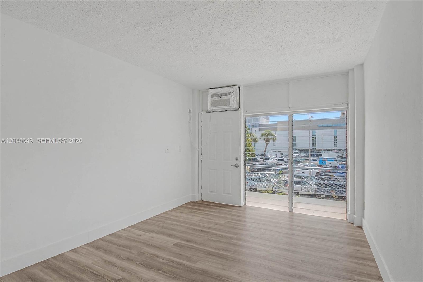 An empty room features white walls, light wood-look flooring, a white door, and a window — 1685 Jefferson Ave # 15, Miami Beach FL 33139, MIAMI BEACH, FL