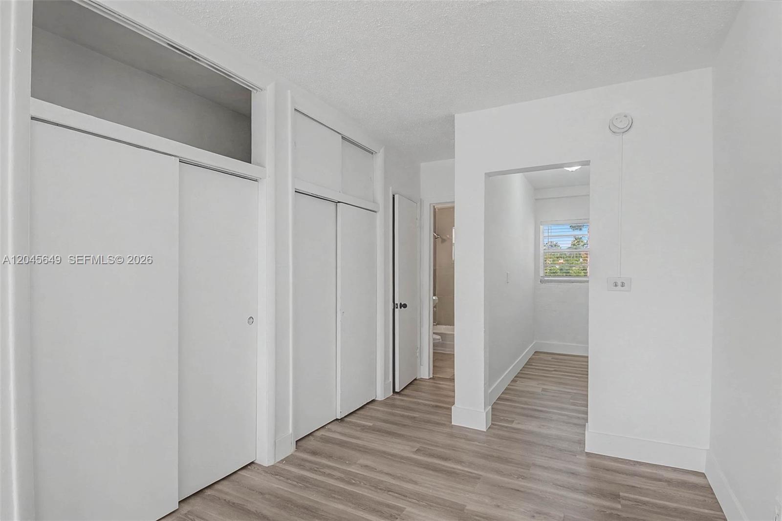 A room with white walls, wood-look flooring, multiple closet doors, and an adjacent bathroom — 1685 Jefferson Ave # 15, Miami Beach FL 33139, MIAMI BEACH, FL